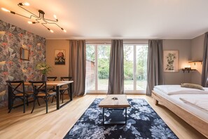 A room with a bed, a dining table with chairs, a small table with a plant, and a large window with curtains. - Design Apartments - "Kutscherhaus" (Potsdam)