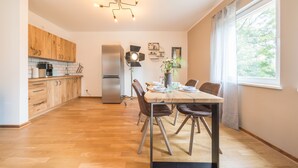 A modern kitchen with wooden cabinets, a stainless steel refrigerator, and a dining area with a table and chairs. - Design Apartments - "Kutscherhaus" (Potsdam)