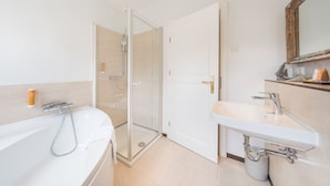 A modern bathroom with a glass-enclosed shower, a white bathtub, and a sink with a mirror above it. - Design Apartments - "Kutscherhaus" (Potsdam)