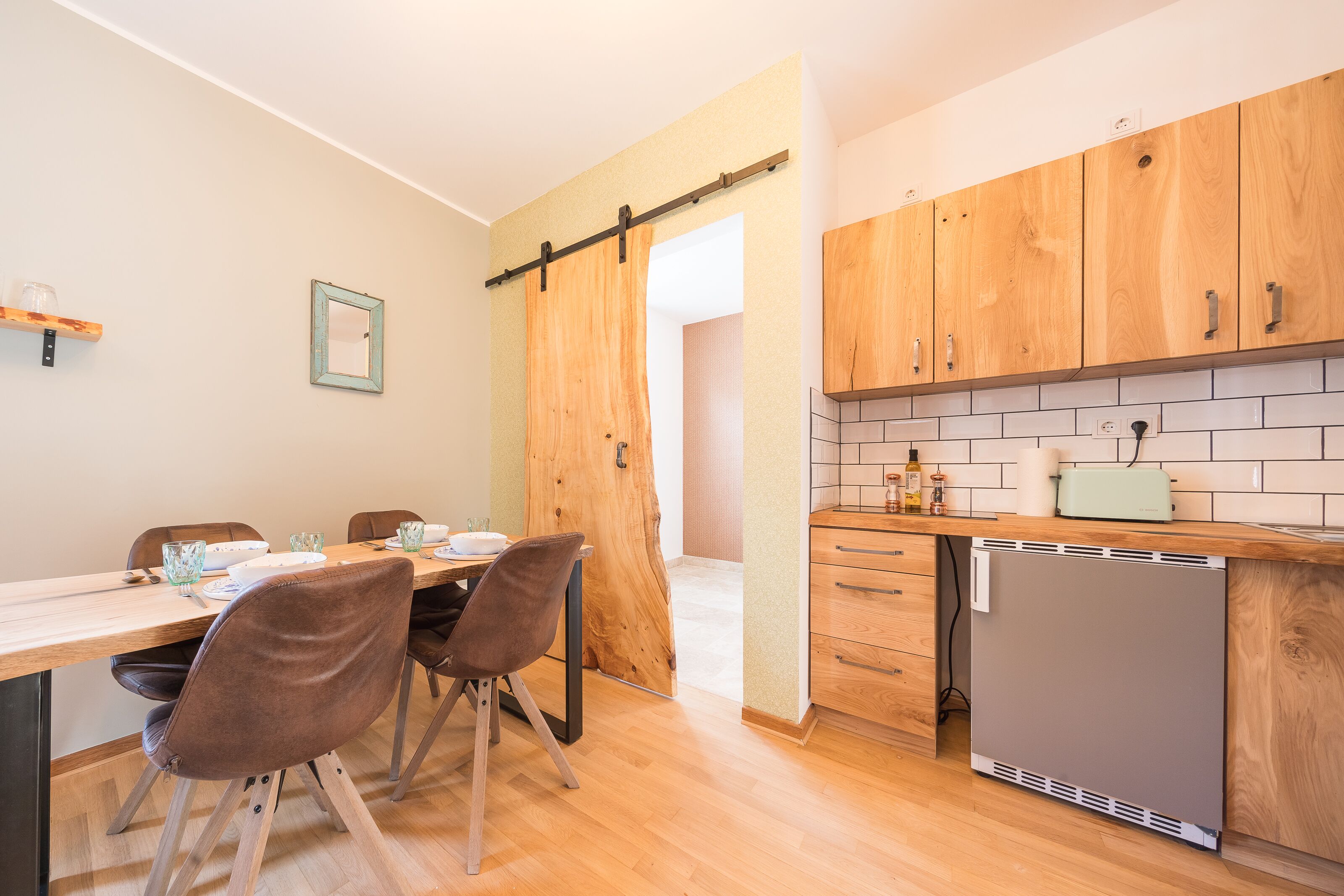 Una cocina moderna con armarios de madera, lavavajillas integrado y una zona de comedor con mesa y sillas de madera.