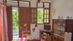 Zona pranzo con tavolo in legno, sedie, tovaglia colorata, un vaso con fiori e una ventola a soffitto.