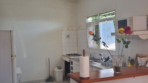 Una cucina con pareti piastrellate di bianco, un fornello, un lavello e una finestra vista verde.