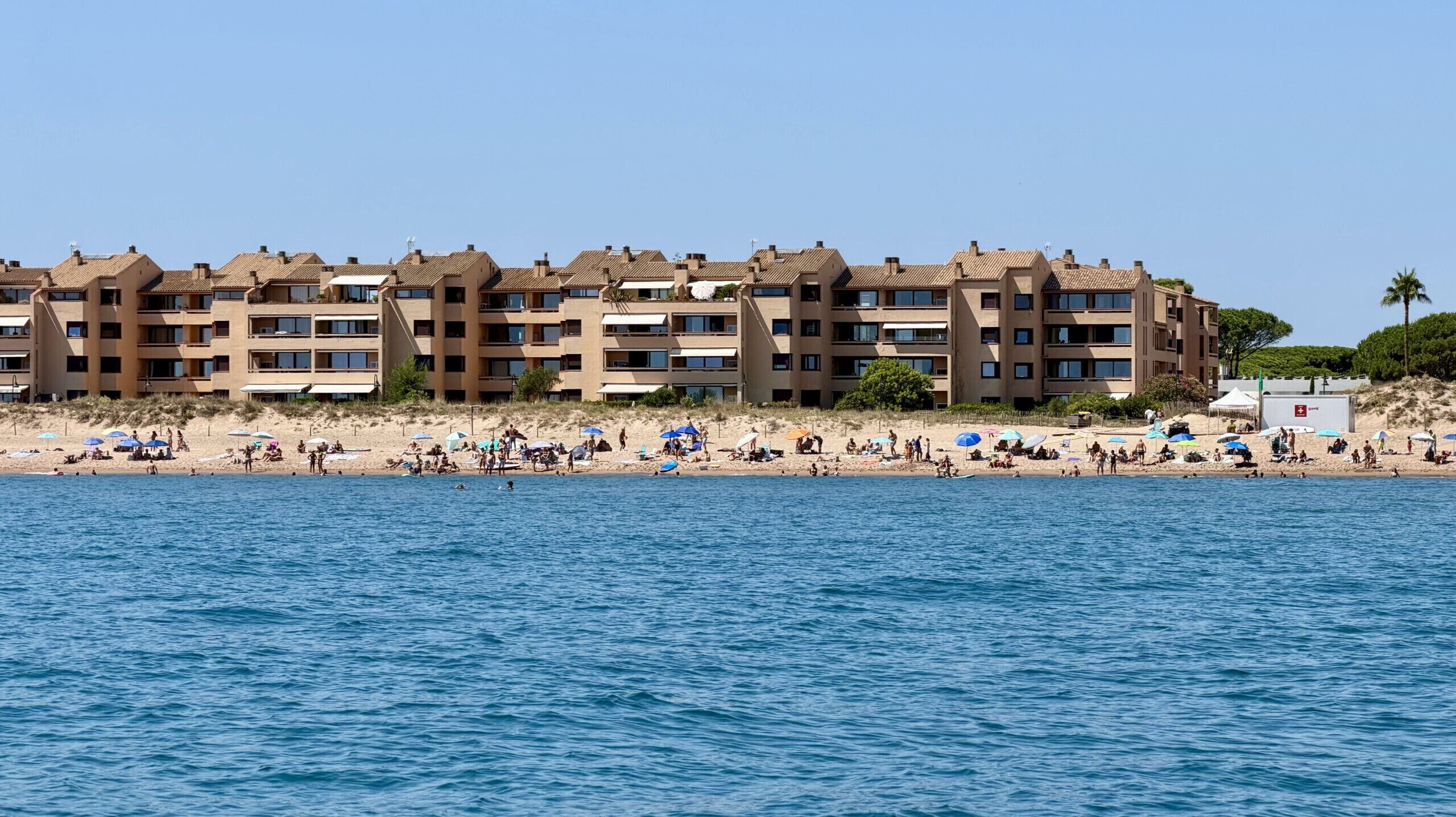 Ein Hotel direkt am Strand mit mehreren Balkonen, einem Sandstrand und einem klaren blauen Meer.