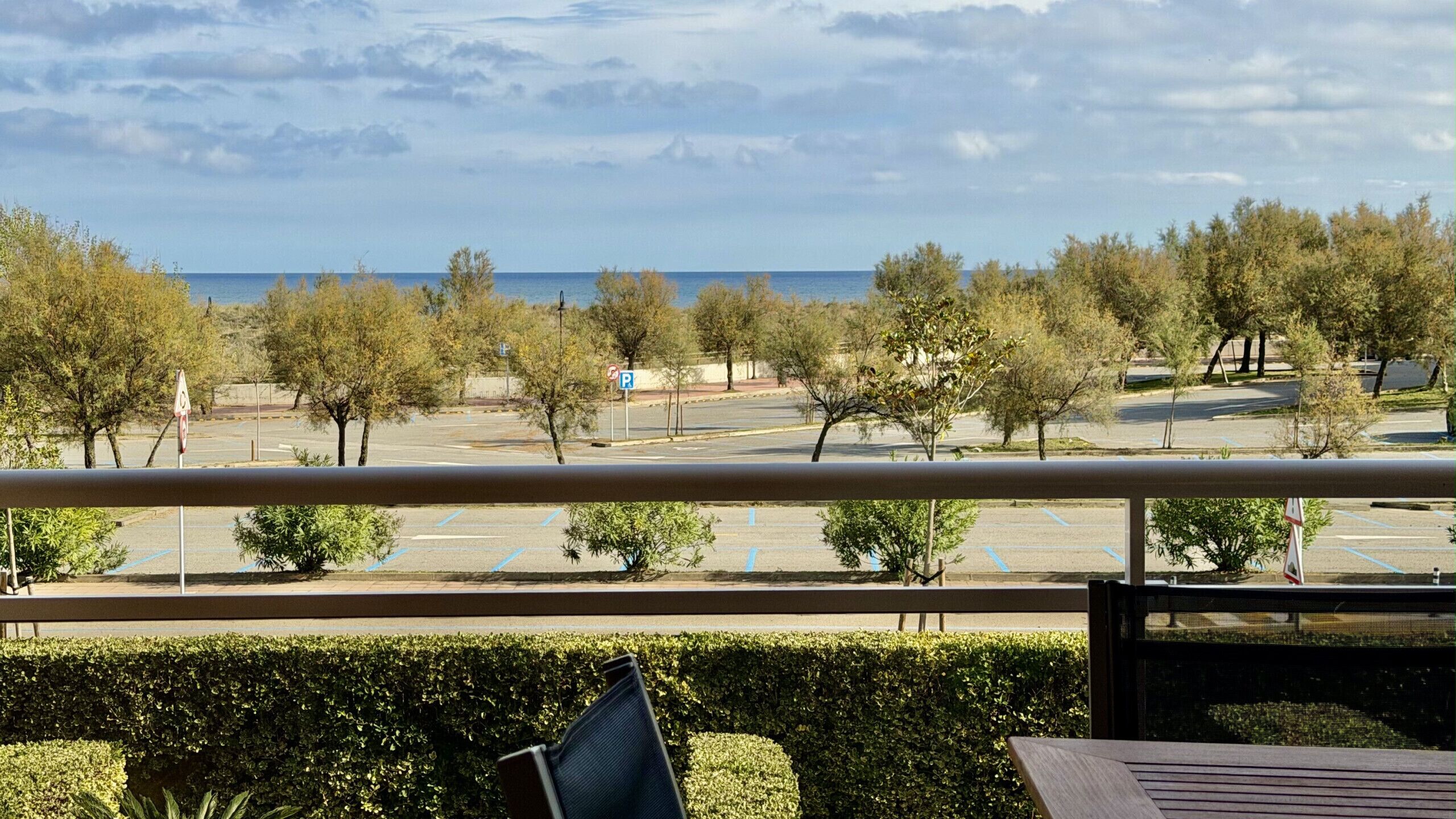 A balcony with a view of a parking lot and trees, overlooking a body of water.