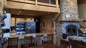 A spacious kitchen with a stone fireplace, wooden upper deck, and modern appliances.
