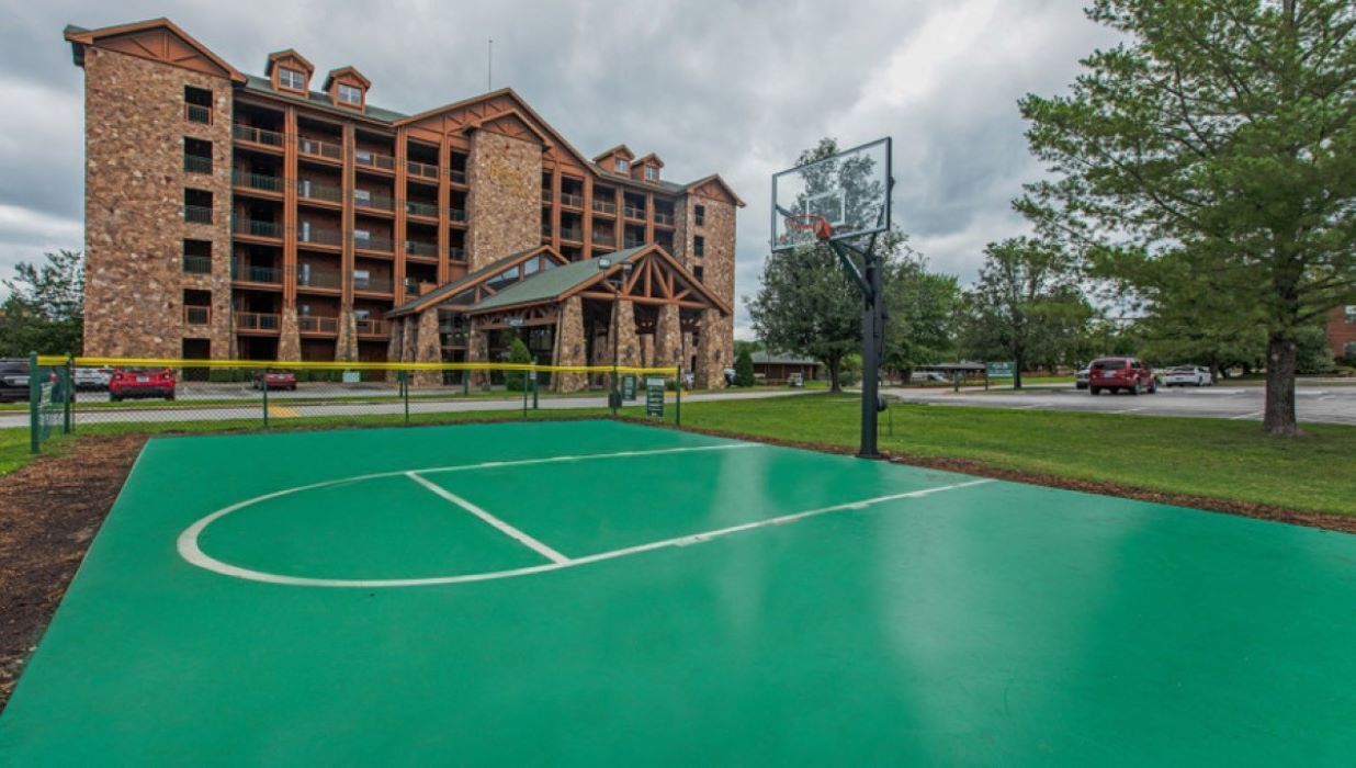 A basketball court adjacent to a multi-story building with a stone facade and wooden accents.