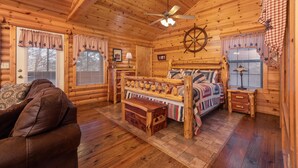 Un dormitorio tipo cabaña de troncos con techo de madera, una cama con cabecera decorativa, un aparador y un banco de madera.