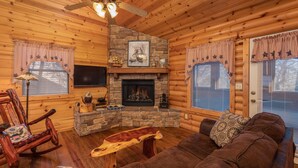 Un acogedor interior de cabaña de madera con chimenea de piedra, muebles de madera y un ventilador de techo.