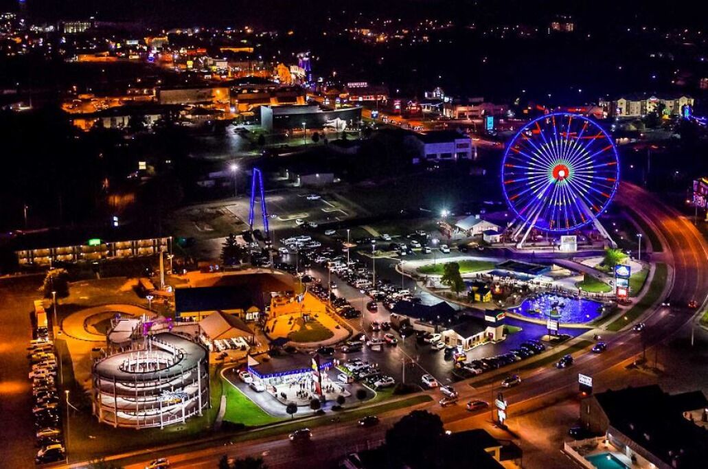 An aerial view of a cityscape at night with a prominent Ferris wheel and a round building with multiple floors.