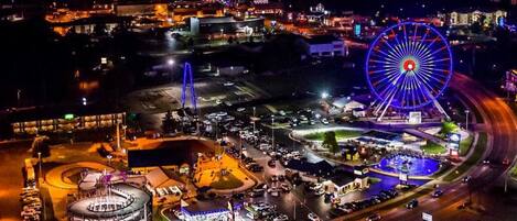 An aerial view of a cityscape at night with a prominent Ferris wheel and a round building with multiple floors.