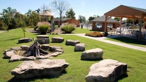 Un parque con un pabellón, mesas de picnic y una hoguera rodeada de rocas.