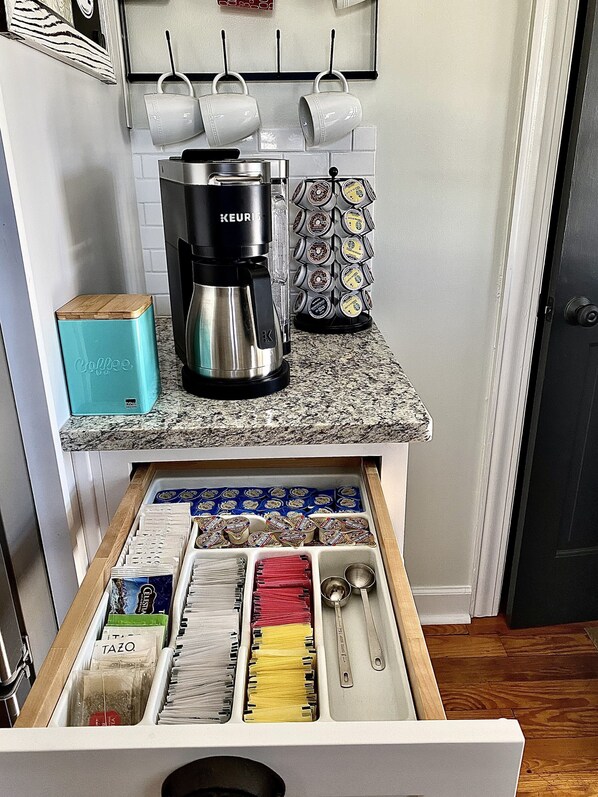 A kitchen with a coffee maker, a drawer with tea bags, and a coffee mug rack.