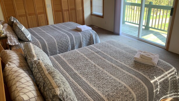 Quarto com duas camas, armários de madeira, janela com persianas e vista para um deck de madeira.
