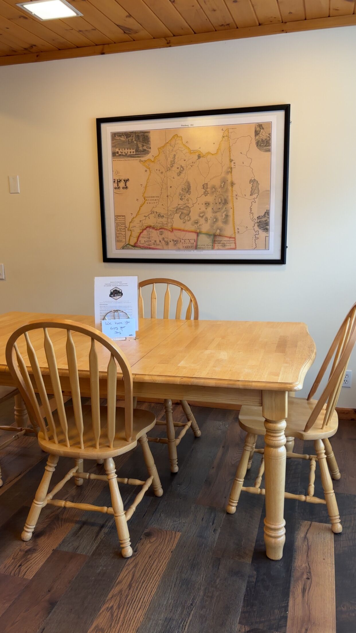 A dining table with four wooden chairs, a framed map on the wall, and a menu sign.