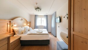 Een slaapkamer met een groot bed, een houten hoofdbord, nachtkastjes, een dressoir, een raam met gordijnen en een televisie aan de muur.