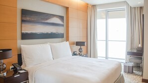 Habitación de hotel con una cama grande, un escritorio, una silla, una mesita de noche, una lámpara, un cuadro en la pared y una ventana con cortinas.
