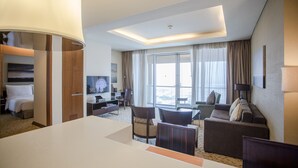 Habitación de hotel con una cama grande, un escritorio, un sofá y un televisor. Tiene un balcón con vistas.