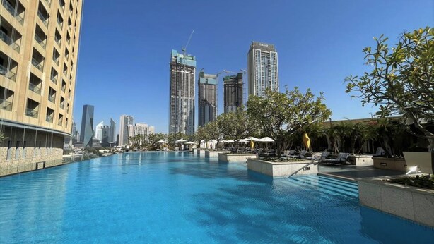 Una piscina con sillas de descanso y sombrillas, rodeada de edificios altos y árboles.