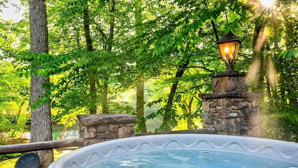 Een hottub omringd door stenen muren en een lantaarnpaal, gelegen in een weelderig, groen bosgebied.