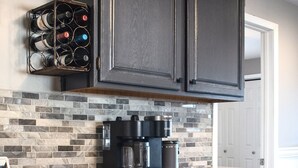 Una cocina con armarios oscuros, encimera de granito, cafetera y una estantería para vinos.