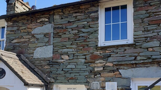 Un edificio de piedra con una puerta blanca con la leyenda "Bottom Shop", un ventanal pequeño y un letrero que indica "4A".