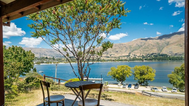 Een houten terras met twee stoelen en een tafel met uitzicht op een meer en bergen op de achtergrond.