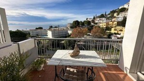 Un balcon avec une table et des chaises, donnant sur une colline parsemée de bâtiments.