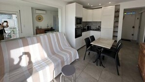 Un espace de vie moderne et compact, comprenant un coin cuisine, un espace repas et un grand lit.