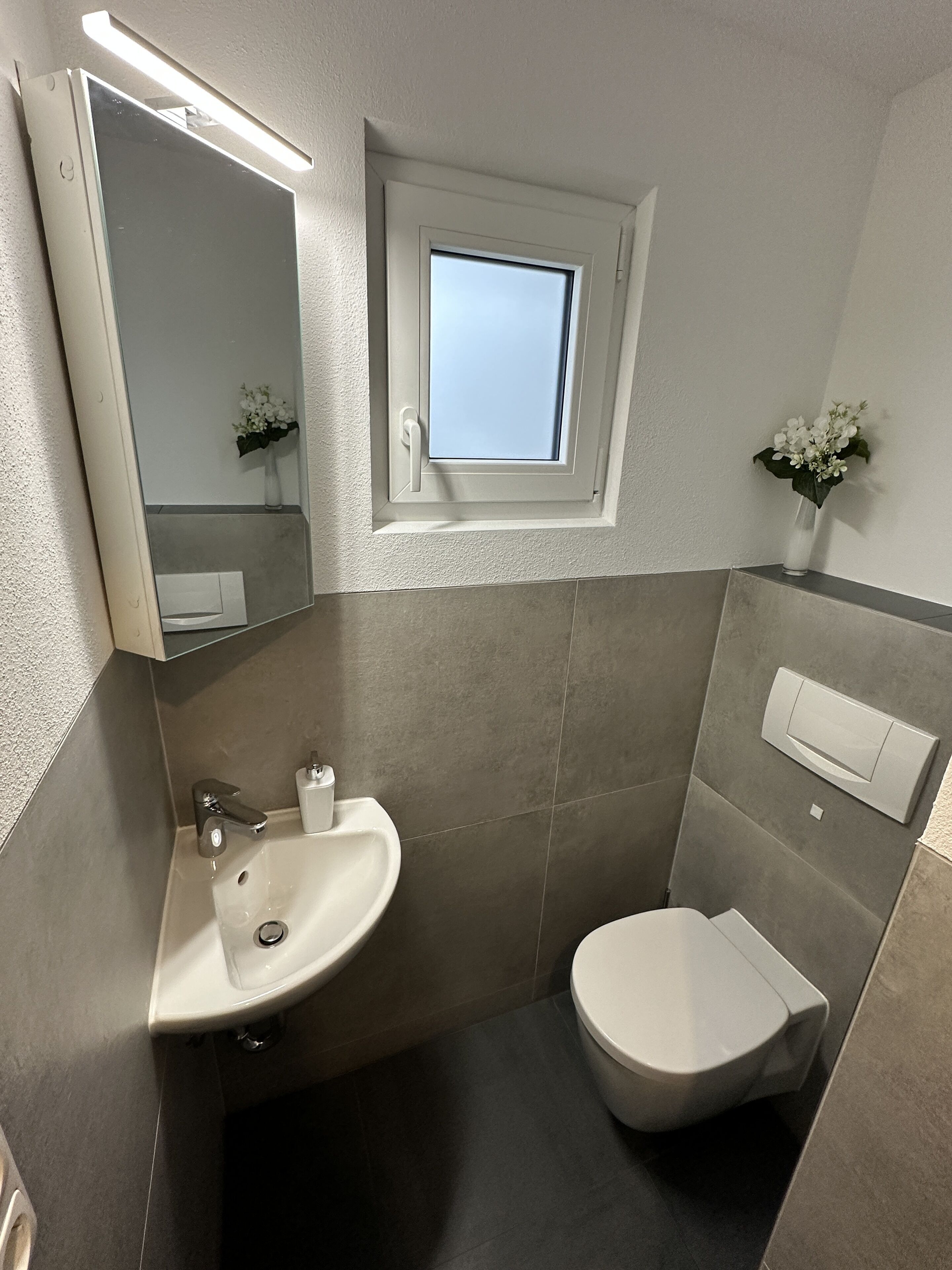A modern bathroom with a sink, toilet, and a small window above the toilet.