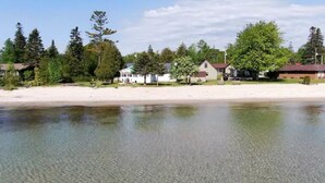 A beachside property with a sandy beach, clear water, and houses in the background.