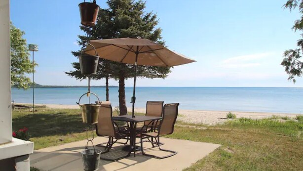 An outdoor patio with a table and chairs, a hanging planter, and a beach view.