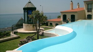 A swimming pool with a curved design, a small tower with a flag, and a view of the sea. - Spacious luxury apartment with 180° ocean view,  pool, seafront beach (Parede)