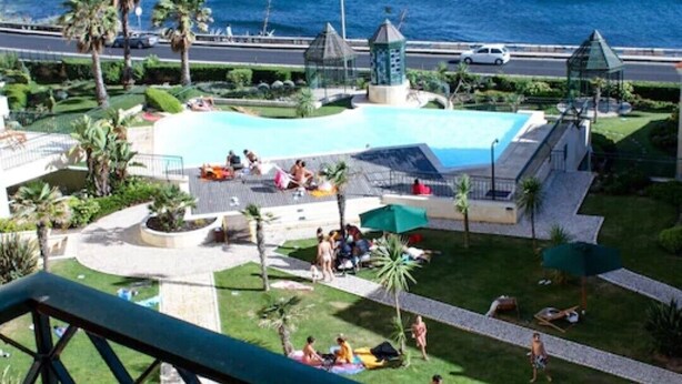A pool area with a view of the ocean, palm trees, and a gazebo. - Spacious luxury apartment with 180° ocean view,  pool, seafront beach (Parede)