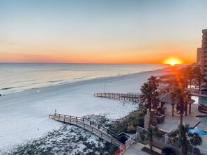 A beach view with a sunset, a wooden boardwalk, and a pool area with palm trees.