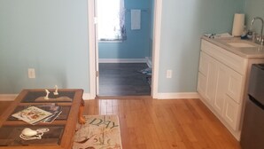 Une pièce dotée d’un plancher en bois, un coin cuisine avec un évier et des placards, une table à manger avec un set de table, et un couloir menant à une autre pièce.