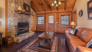 A log cabin interior with a stone fireplace, wooden ceiling beams, a leather sofa, and a stone wall. - "Fox Trail" Luxury cabin at Branson Woods Resort (Branson)