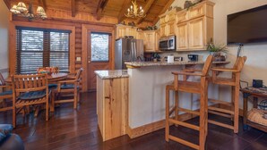 A wooden kitchen with a central island, bar stools, and a dining table with chairs. - "Fox Trail" Luxury cabin at Branson Woods Resort (Branson)