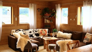 L’intérieur d’un chalet chaleureux, avec des murs en bois, un canapé marron, une table basse et une bibliothèque remplie de livres et de plantes.