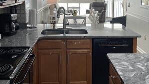 A modern kitchen with granite countertops, wooden cabinets, a built-in dishwasher, and a central island with a sink. - Stunning Top-Floor 3 Bedroom, 2 Bath Oceanfront Condo 902 Pinnacle (North Myrtle Beach)