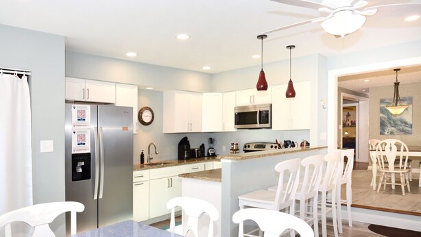 A modern kitchen with white cabinets, a stainless steel refrigerator, a microwave, and a dining area with white chairs and a table. - Pet Friendly Downtown Rehoboth Beach House (Rehoboth Beach)