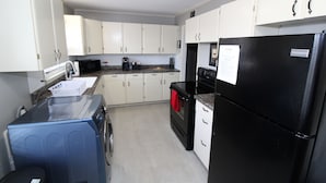 Una cocina compacta con armarios blancos, un refrigerador negro, un microondas y una lavadora.