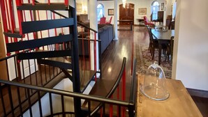 A modern interior with a spiral staircase featuring red and black railings, a dining area with a wooden table and chairs, and a cozy seating area with a sofa and armchairs.