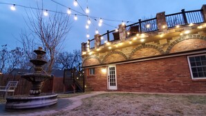 A brick house with a stone staircase, a wooden deck, and a fountain in the yard.