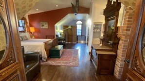 A spacious loft bedroom with a large bed, a sitting area with a green ottoman, and a dining area with a table and chairs.