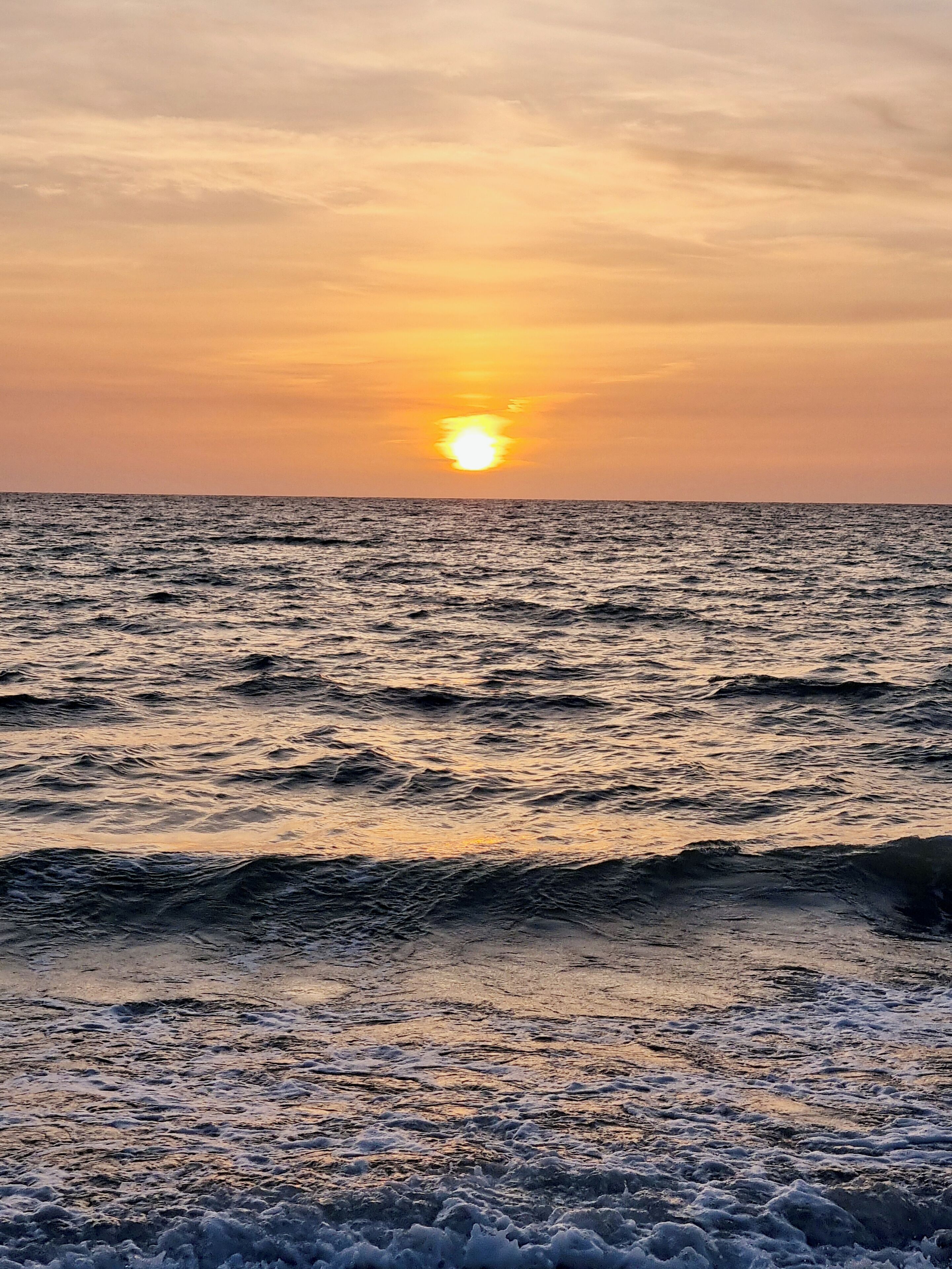 A sunset over the ocean with waves approaching the shore.