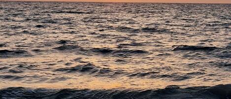 A sunset over the ocean with waves approaching the shore.