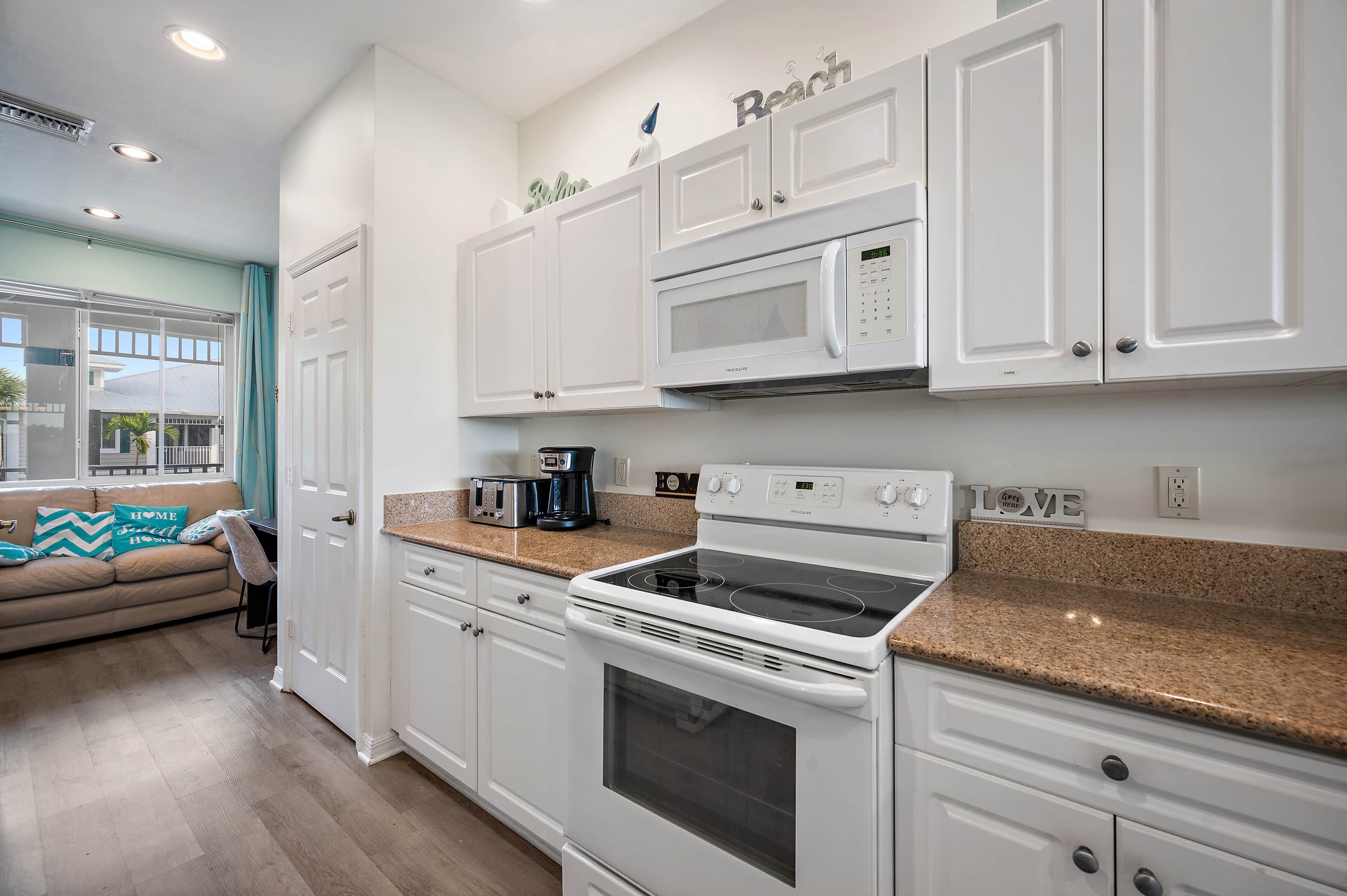 A modern kitchen with white cabinets, a granite countertop, a built-in microwave, a stove, and a coffee maker.