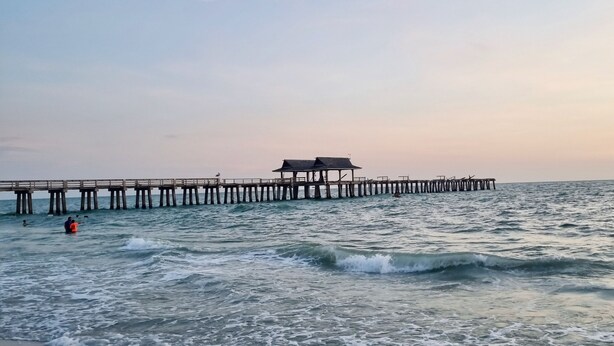 Ein Strand mit einer hölzernen Pier, die sich ins Meer erstreckt.