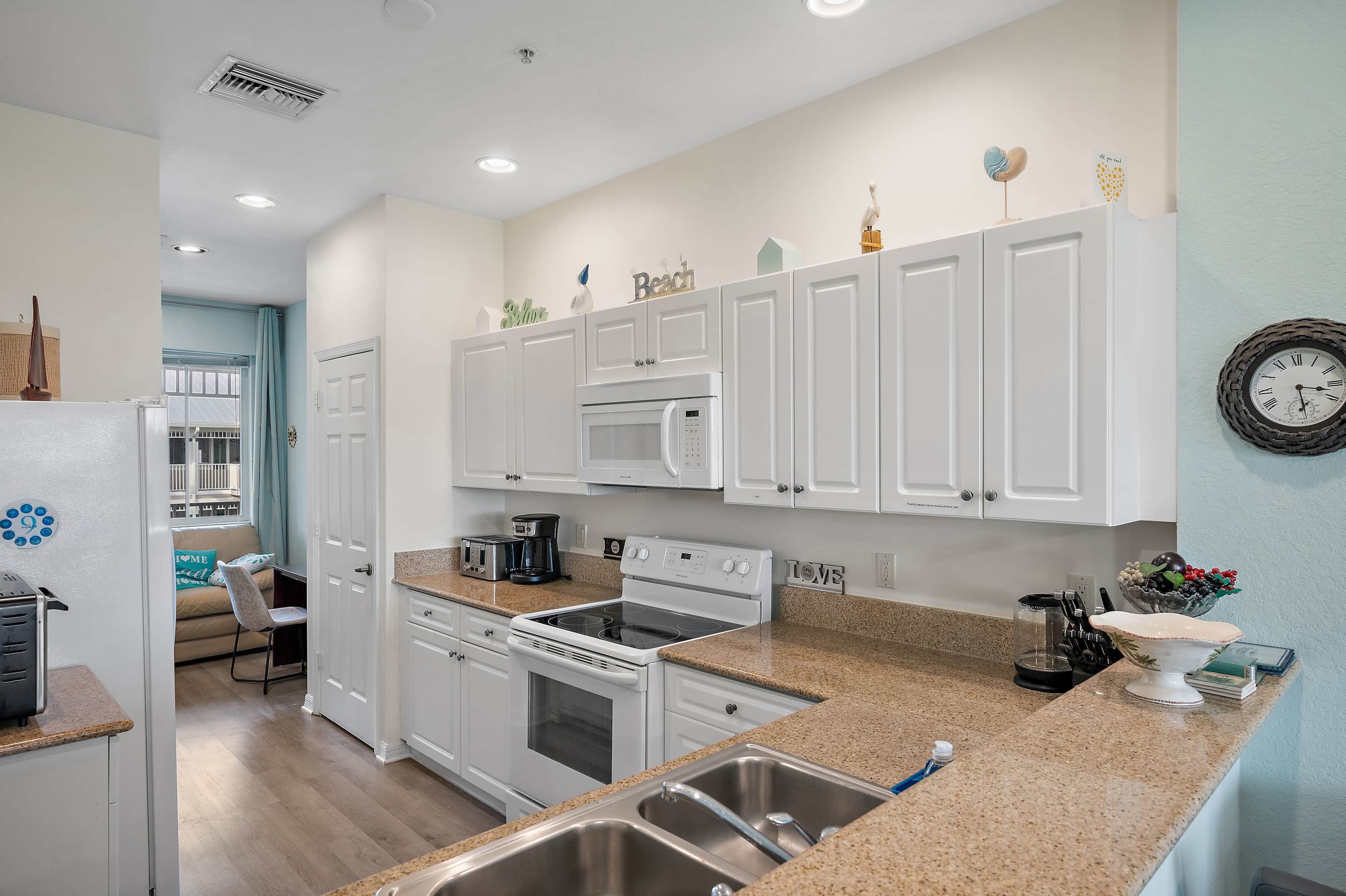 Una cocina moderna con armarios blancos, microondas, estufa y lavaplatos. Hay un comedor con mesa y sillas.