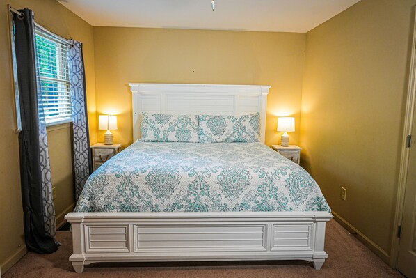 A bedroom with a white bed, two bedside lamps, a patterned bedspread, and a window with curtains. - One of a kind our Mini Lodge Chalet directly across from our pool! (Pine Mountain)